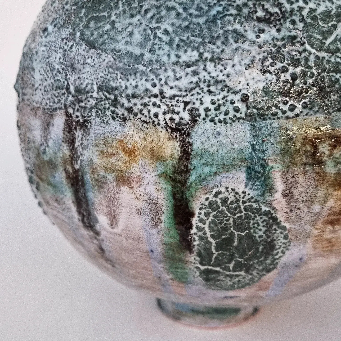 Close up of Large ceramic round sphere vase with green and white melted glaze