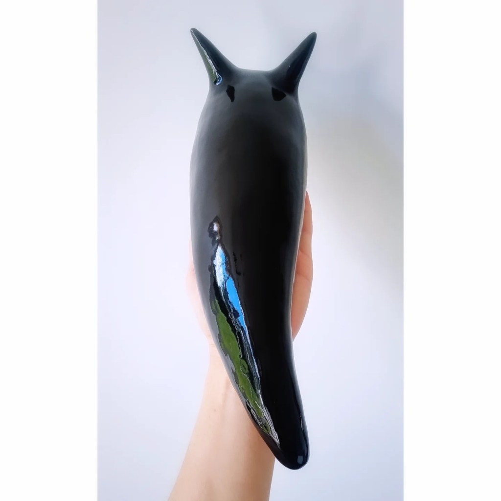 Giant black glossy slug being held up by a hand on a white background